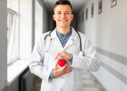 Médico segura uma miniatura de coração e um estetoscópio, simbolizando como prevenir doenças cardiovasculares.