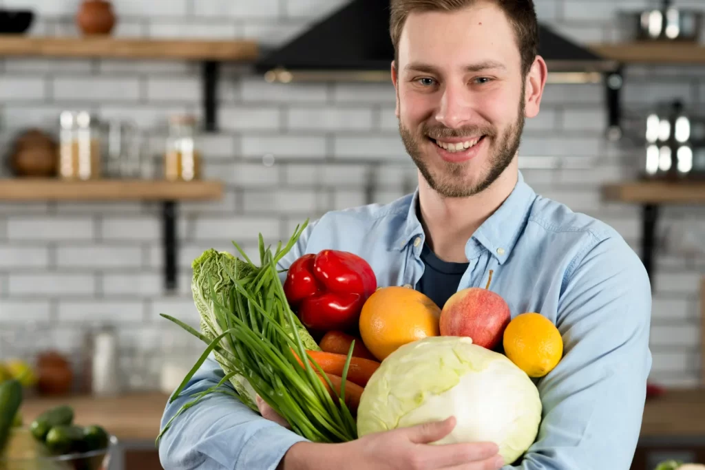Homem na cozinha segura legumes, frutas e vegetais essenciais para alimentação saudável para coração