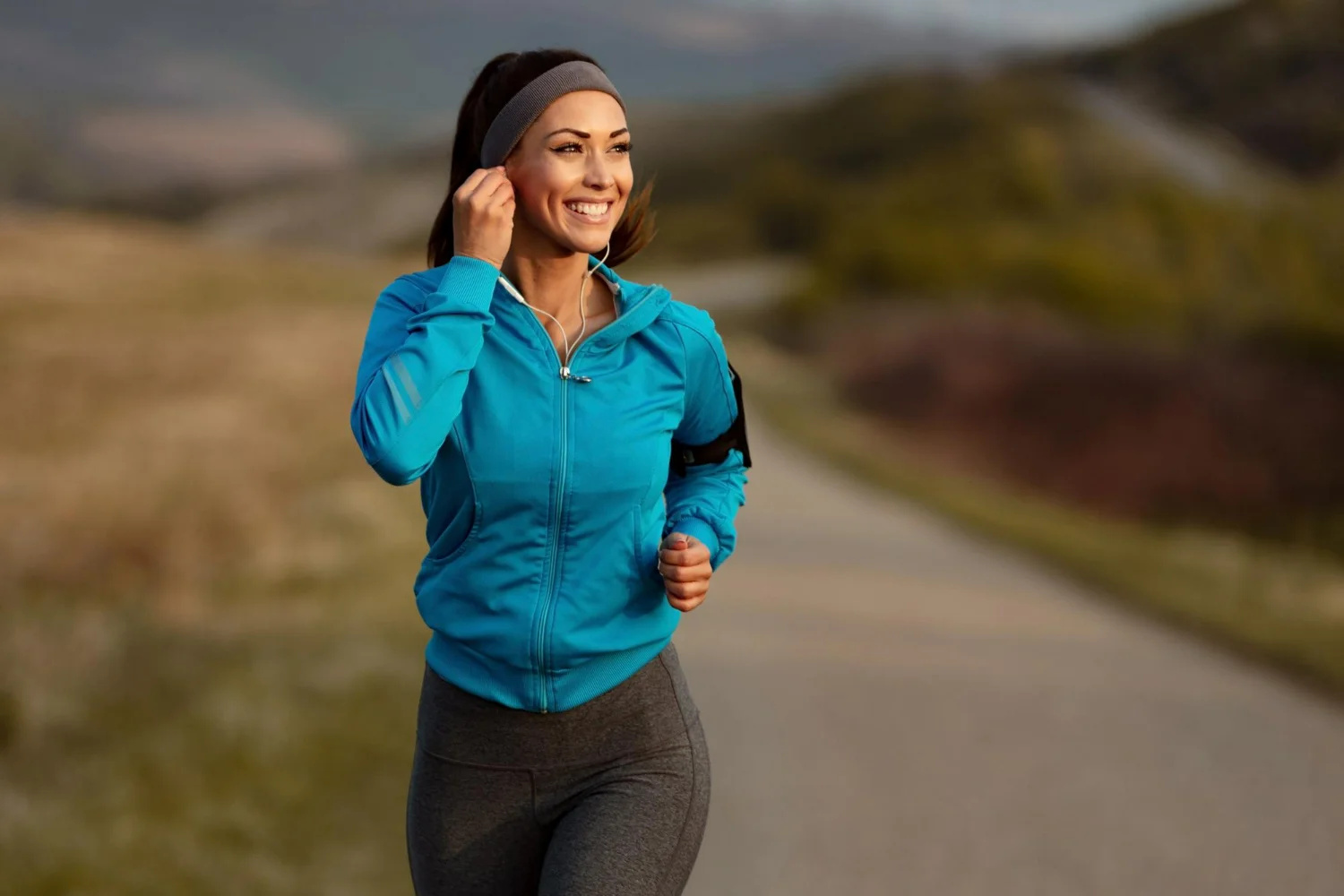 Mulher sorridente com roupa de ginástica corre em estrada porque correr faz bem para coração