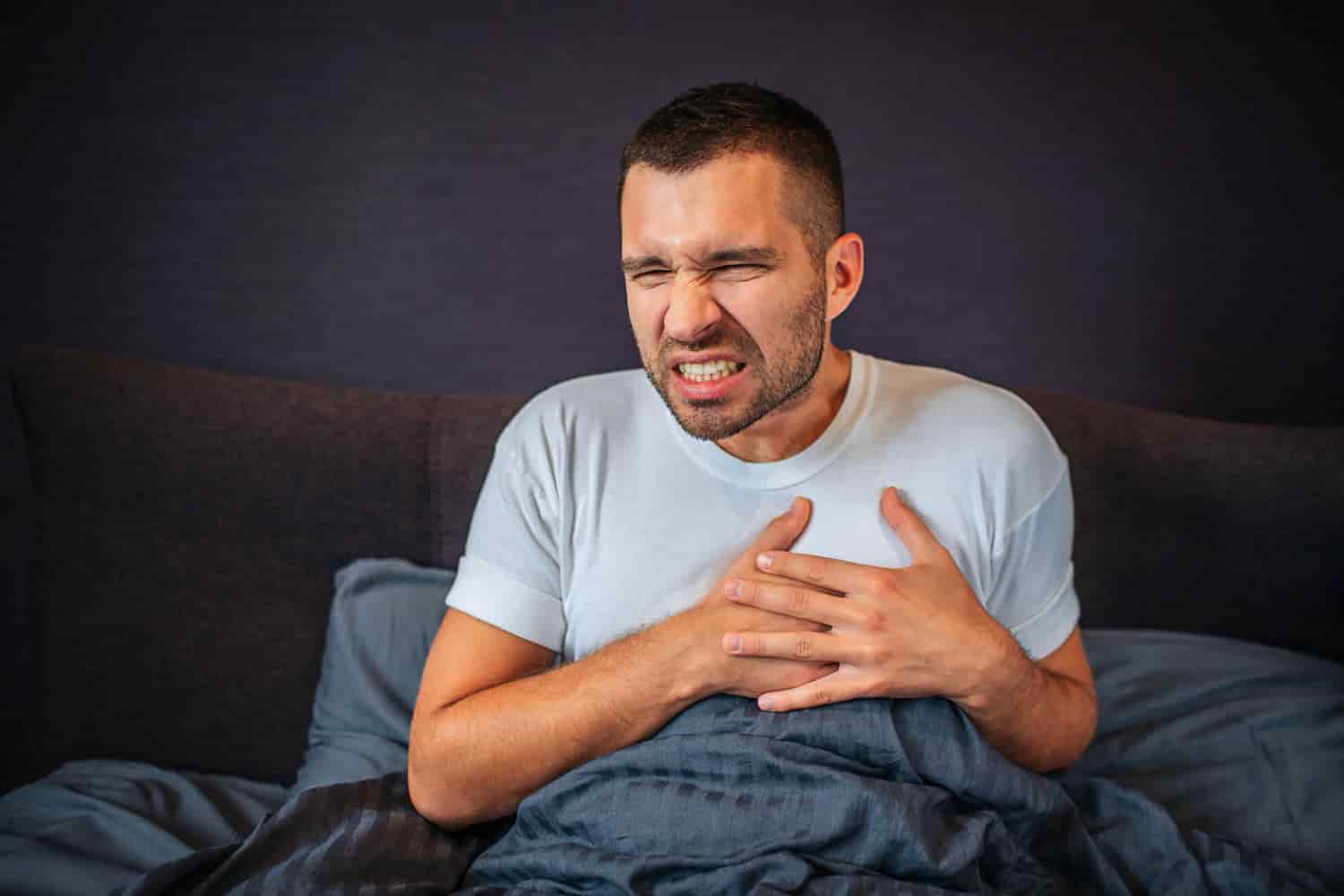 Homem na cama segura o peito com coração acelerado ao acordar
